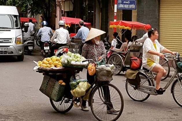 Eine Obstverkäuferin mit Fahrrad und mit dem vietnamesischen Kegelhut.