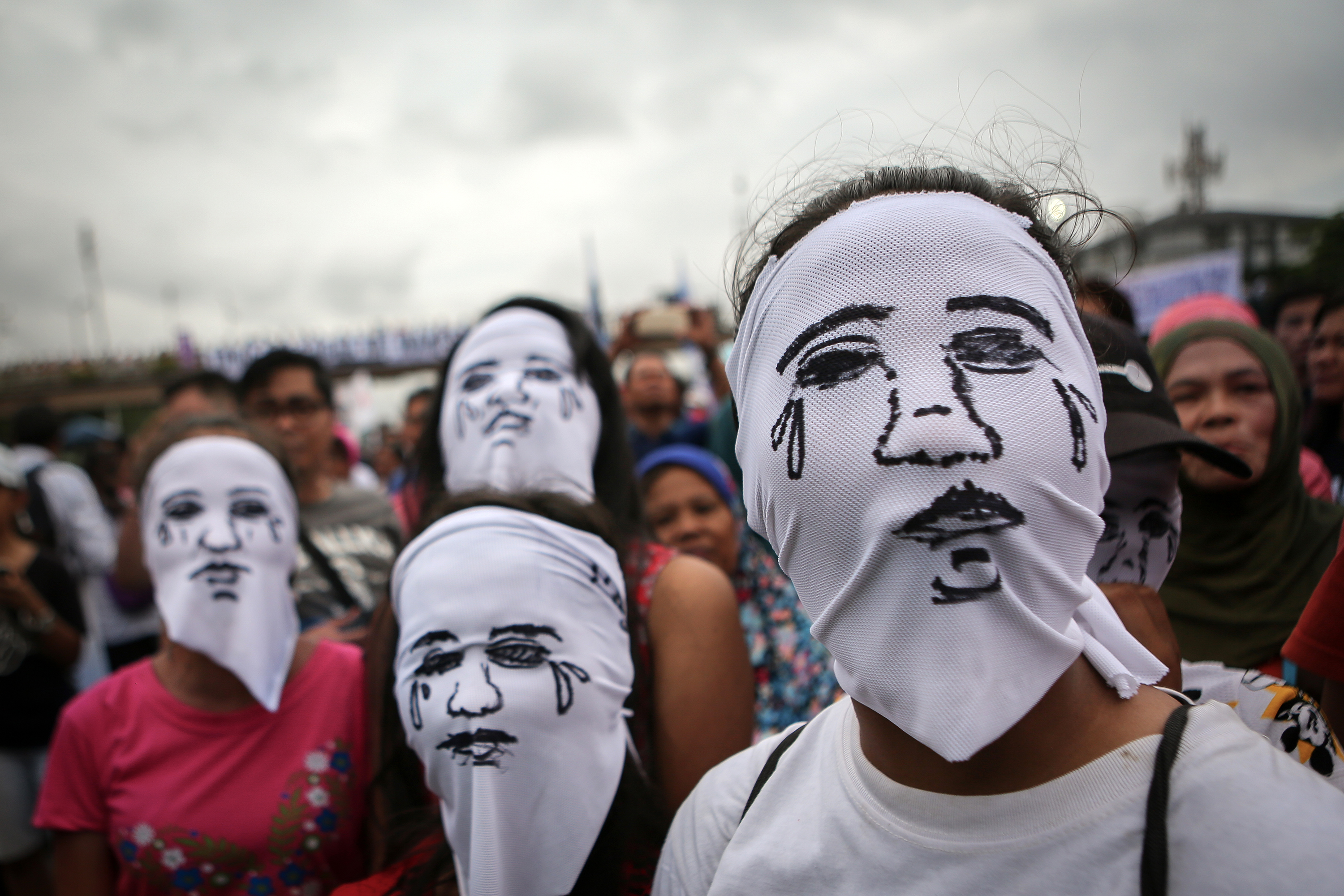 Anonymous protest of relatives of murder victims In front of a crowd are standing four persons. Each is wearing a white cloth, with a crying face drawn on it, over the head.